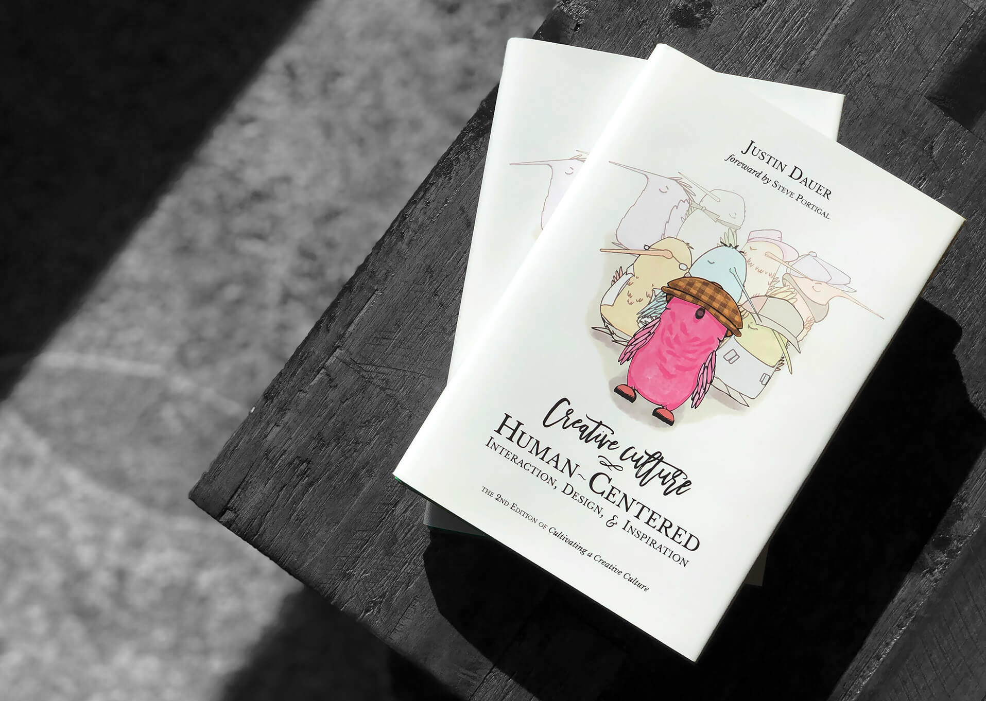 a couple copies of the hardcover book Creative Culture: Human-Centered Interaction, Design, and Inspiration resting on a wood table
